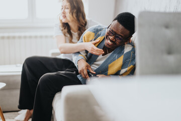 A cheerful moment between a diverse couple relaxing in a modern living room, showcasing joy, connection, and togetherness in a casual home environment.