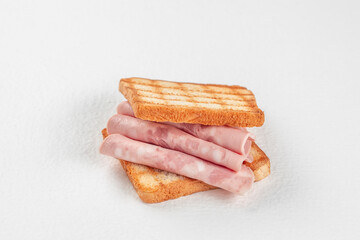 Rolled slices of deli ham are stacked between two pieces of golden grilled toast, creating a simple...