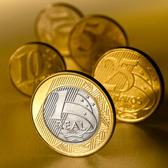 Moeda de 1 Real em primeiro plano com moedas de menor valor ao fundo.