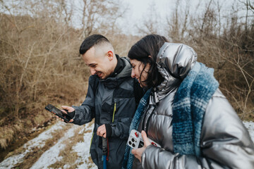 Friends sharing a lighthearted moment in nature, laughing while using a smart phone together on a cold winter day surrounded by a serene woodland background.