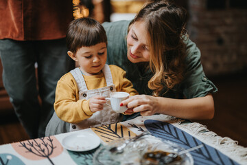 A caring mother engages with her young child, guiding them in a cozy and warm home environment.