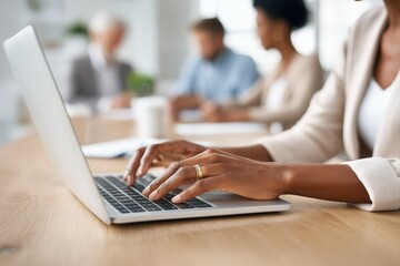 Close-up of hands typing on a laptop keyboard in an office with blurred business people working together.