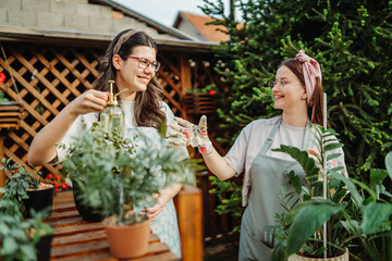 Two female friends or sisters taking care of plants with water can and mister	

