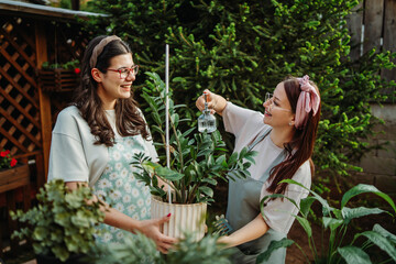 Two female friends or sisters taking care of plants with water can and mister	
