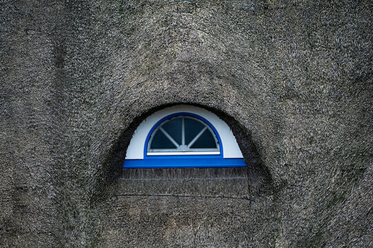 A round window in the roof of a thatched roof house in Germany.