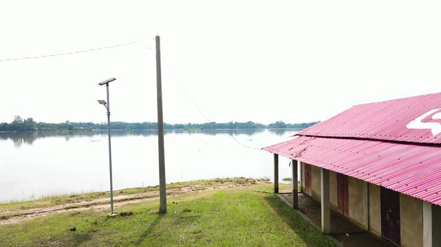 An Electric Pole Stands Beside a Rural House Surrounded by Floodwaters in the Haor Area of Sylhet, Bangladesh, South Asia - Pan Down Shot