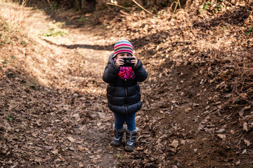 Little girl taking pictures in a forest trail during winter