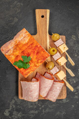 Sliced ham with a paprika crust is elegantly arranged on a wooden board alongside cheese cubes,...