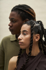 Young Black woman and young Caucasian woman standing close together facing sideways, both with...