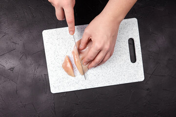 Hands of a person slicing fresh chicken breast on a modern cutting board, showcasing culinary...