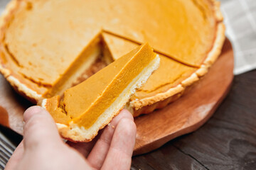 Delicious pumpkin pie on a wooden board with a slice being served, showcasing the creamy filling and golden crust, perfect for autumn gatherings and festive celebrations