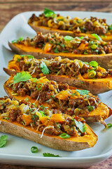 baked sweet potatoes stuffed with chorizo sausage, cheddar cheese, chipotle sauce, and green onions, close up