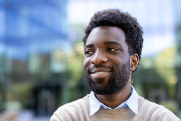 A smiling African American man looking off to the side, with a blurred building in the background.