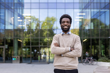 A smiling man in front of a modern office building, arms crossed, looking confident and professional. The background includes a bicycle.