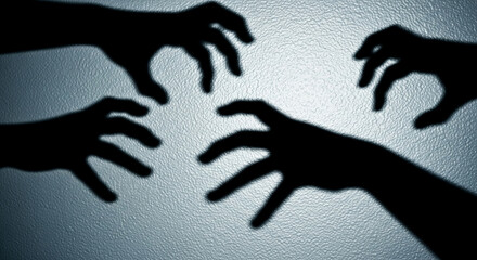 Four dark hand shadows projected on a textured light-blue surface, creating a mysterious and suspenseful atmosphere, symbolic of fear, threat, or unseen presence