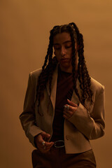 Young adult Black woman standing with eyes closed, wearing rings and holding jacket lapel, long...