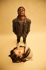 Black teenage boy standing with hands in pockets looking down, while Hispanic teenage girl with...