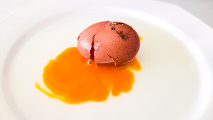 Cracked brown egg with yolk on white plate