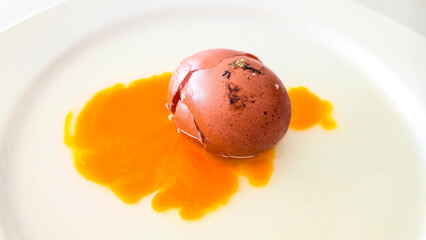 Cracked brown egg with yolk on white plate