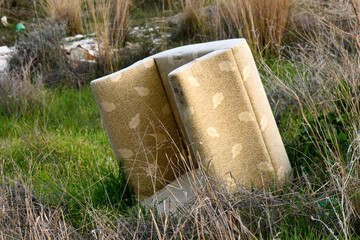 Single, tattered, and discarded old sofa cushion with  faded floral pattern lies abandoned in a...