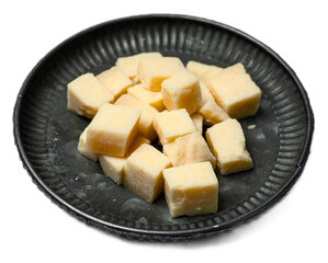 Diced parmesan cheese cubes with aged italian flavor on black ceramic plate isolated on transparent background