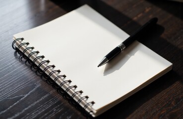 A blank spiral notebook with a pen resting on top placed on a dark wooden surface