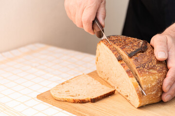 Freshly baked bread being sliced on a wooden cutting board during a home cooking session in a cozy...