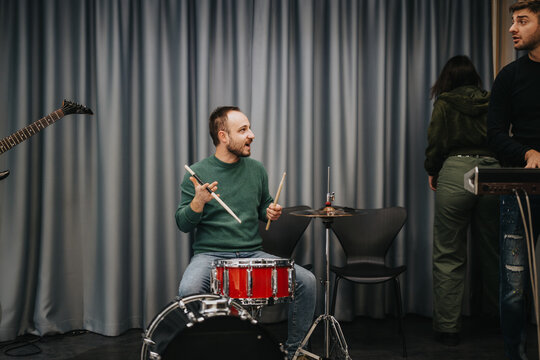 A diverse group of musicians engaging in a lively band practice session. Instruments like drums, guitar, and keyboard are visible, capturing the excitement and creativity of making music together. - Powered by Adobe