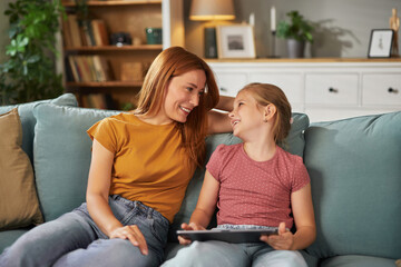 A woman and a girl are sitting on a comfortable couch in a well-decorated living room, engaging in...