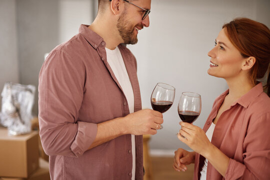 Couple enjoys a toast with glasses of red wine while surrounded by moving boxes in their new living space, sharing smiles and excitement for their fresh start.