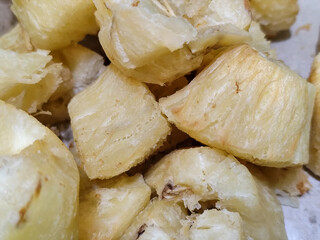 Fried cassava, golden yellow in color and crispy texture can be seen filling the entire frame, showing details of the fibers and soft inside