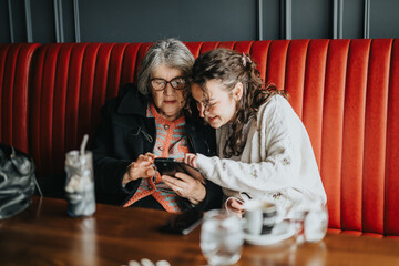 An elderly woman and a younger woman enjoy bonding while sharing moments using a smart phone,...