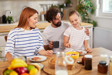 Family members sit together at a wooden table sharing breakfast. Delicious food is displayed, and laughter fills the cozy kitchen as they bond in this warm moment.