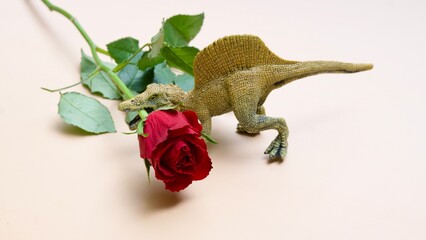 Ein Spielzeugdinosaurier hält eine rote Rose im Maul. Geschenk, Geburtstag, Jubiläum.