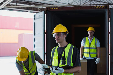 Group of warehouse workers in safety vests and helmets loading boxes into cargo container inside distribution center under natural lighting.