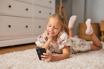 A young girl lies comfortably on a white rug, propping herself up on her elbows while smiling at...