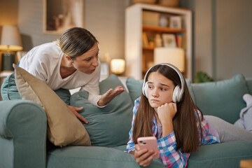 A mother sits on the couch expressing her feelings with strong gestures to her teenage daughter,...