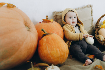 Adorable baby boy sitting on blanket with pumpkins,  autumn leaves and flowers. Autumn harvest and Happy Thanksgiving. Cute happy child with fall decor at home