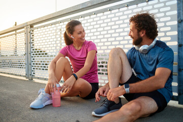 After finishing a workout, two friends sit on a bridge, sharing a moment of laughter. They enjoy...