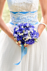 An elegant bride holds a beautifully arranged bouquet of blue and white flowers, enhancing the...
