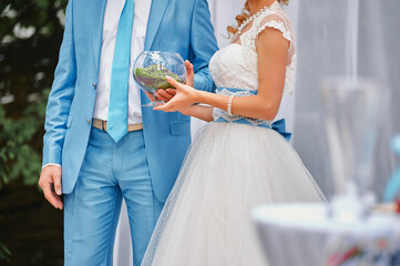 Bride and groom dressed elegantly during a wedding ceremony, focusing on the terrarium bowl with a...