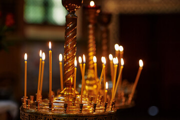 A beautifully illuminated golden orthodox church candlestand holds numerous prayer beewax candles,...