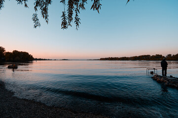 Man Standing by Lakeshore During a Serene Sunset at Twilight