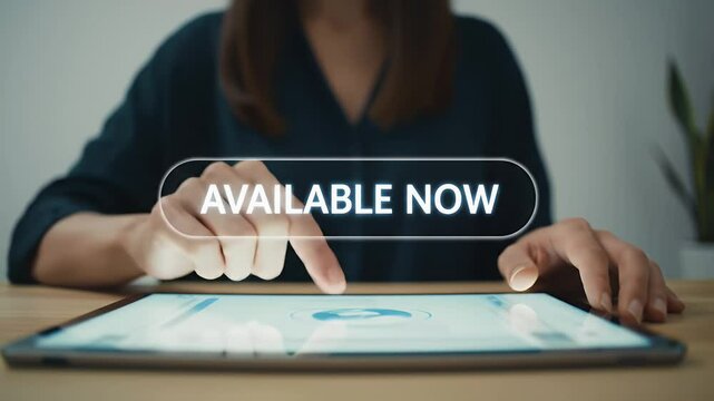 Woman in Dark Green Shirt Touching Tablet with Available Now Sign on Screen In Office Setting on Wooden Table