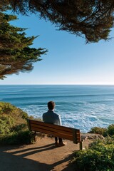 Young male enjoying ocean view from cliffside bench on sunny day