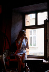 Woman Enjoying a Coffee by a Window in Dimly Lit Cafe