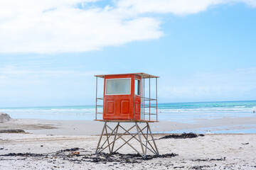 Ein roter Rettungsschwimmer-Turm steht verlassen an einem weiten Sandstrand mit dem Meer und einem...