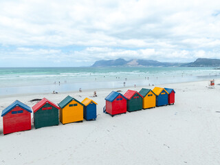Weite Ansicht des Muizenberg Strandes mit bunten Strandhäuschen im Vordergrund, dem Meer und...