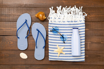 Beach towel with summer accessories on wooden background, top view