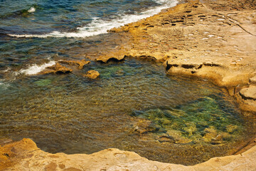 A serene rock pool with crystal-clear seawater and visible salt deposits in smooth Mediterranean stone under warm sunlight. Ideal for nature, travel, and geology themes.
